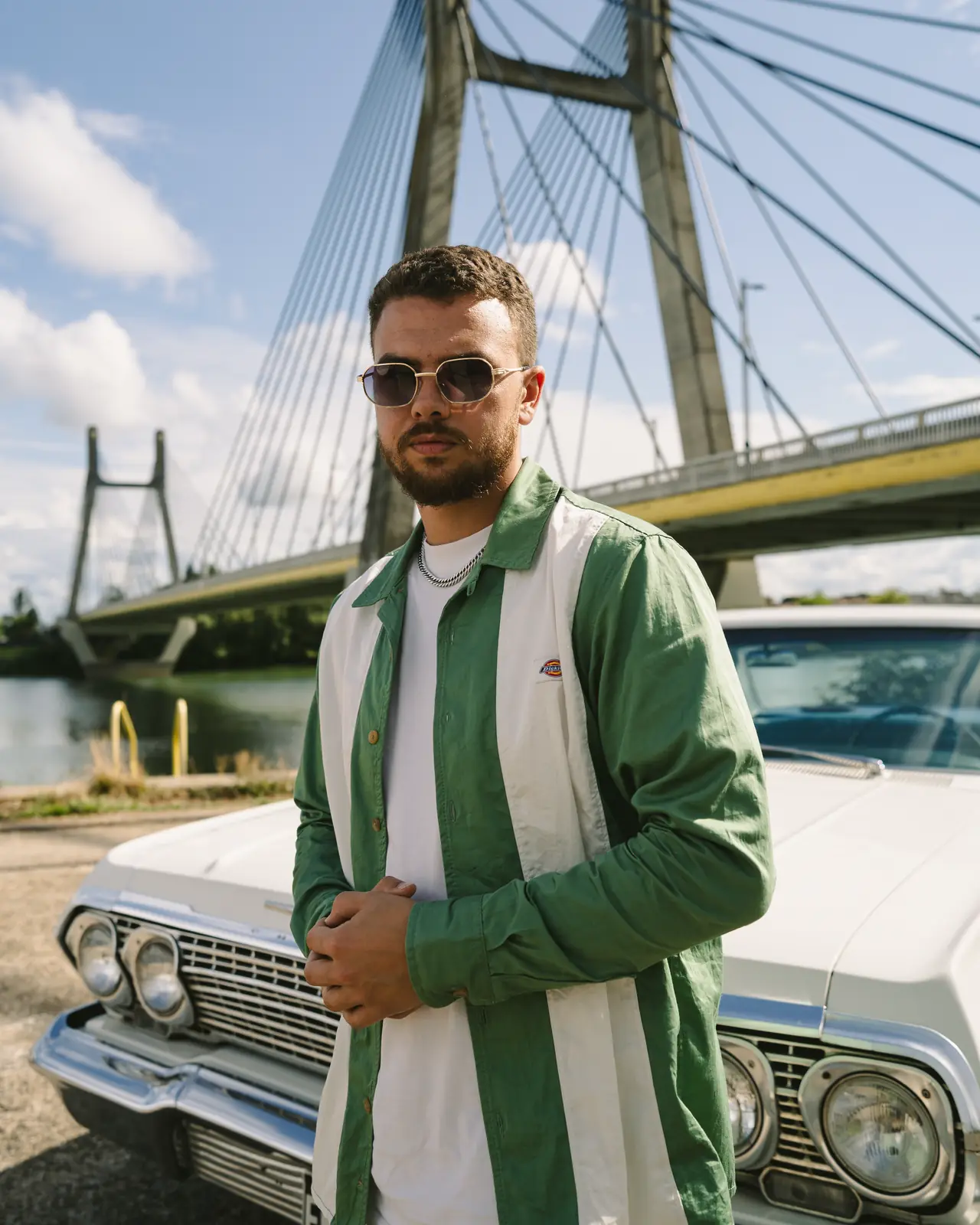 SOB debout devant une Impala blanche, sous un pont à haubans
