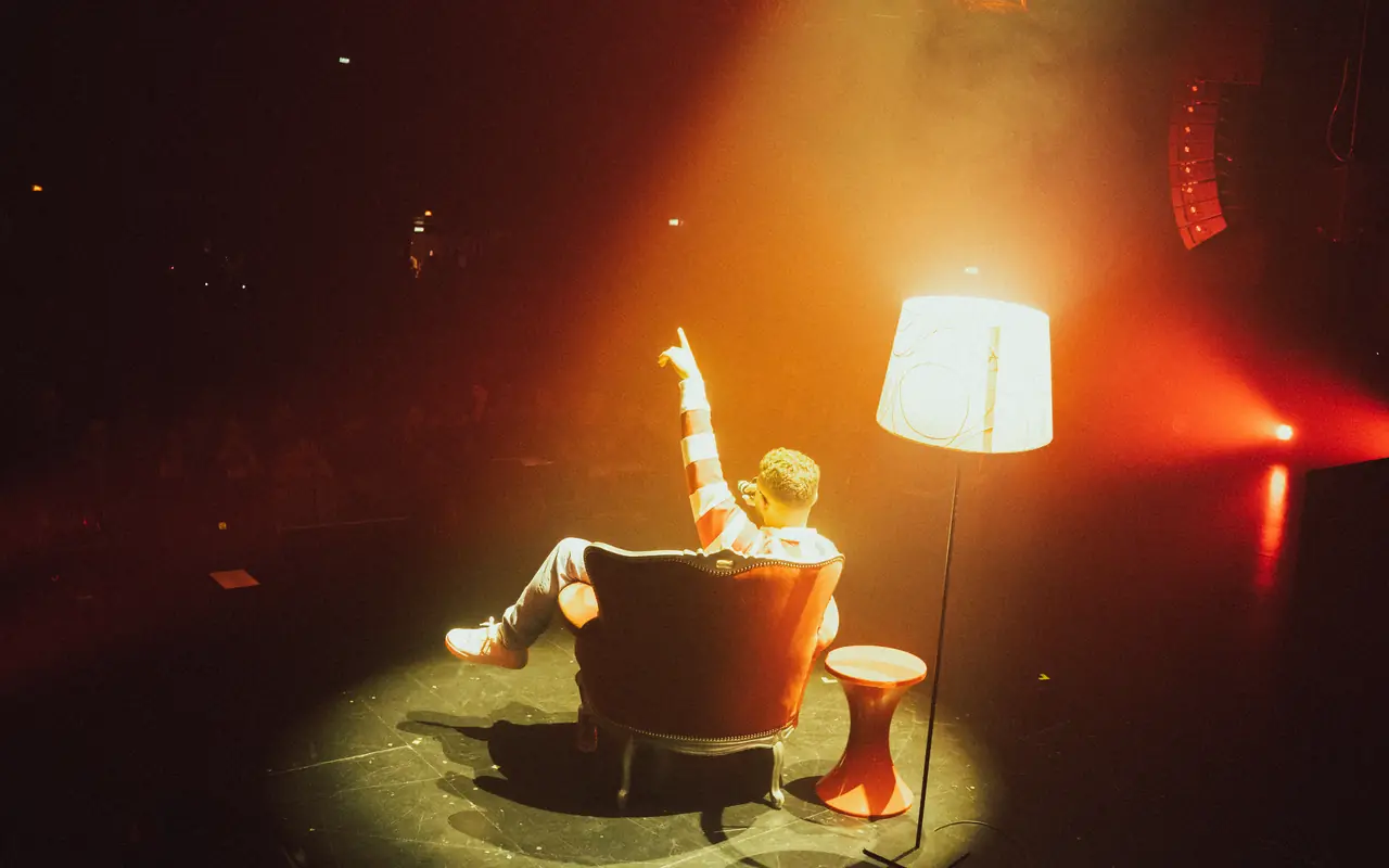 SOB assis dans un fauteuil sur scène, sous une lampe